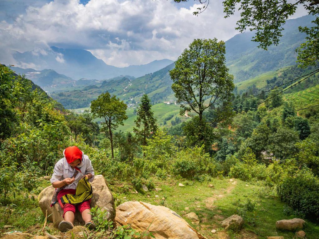 Red Dzao woman sewing traditional clothing